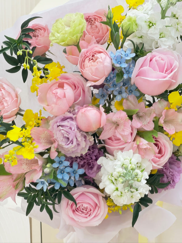 Romantic pastel flower bouquet featuring soft pink roses, white stock, purple lisianthus and cheerful yellow orchids