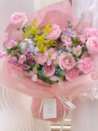 Pastel garden bouquet with pink roses, yellow alstroemeria and mixed seasonal flowers in pink wrapping