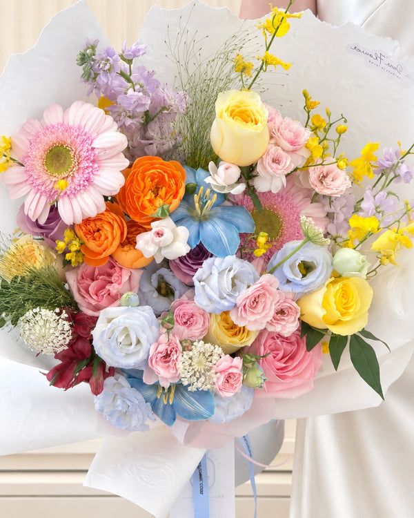Vibrant mixed flower bouquet featuring pink and yellow roses, purple Matthiola, yellow orchids and pastel blue blooms