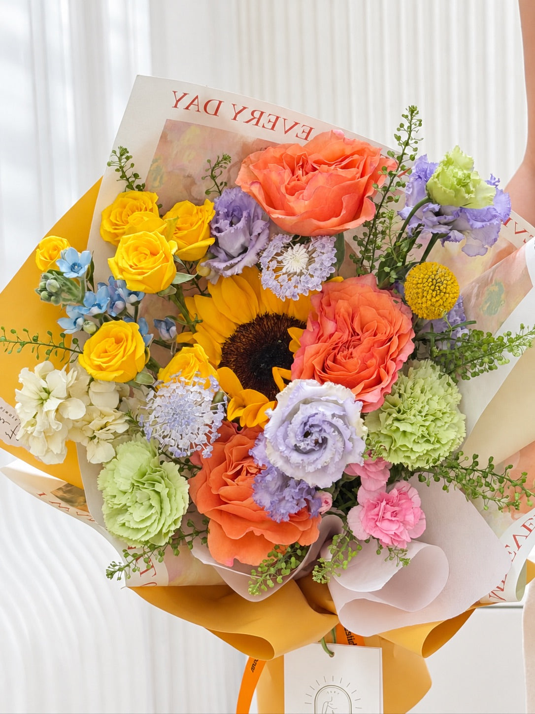 Close-up of Chasing Dreams graduation bouquet with sunflower, coral orange roses, yellow spray roses, lavender lisianthus and green carnations.