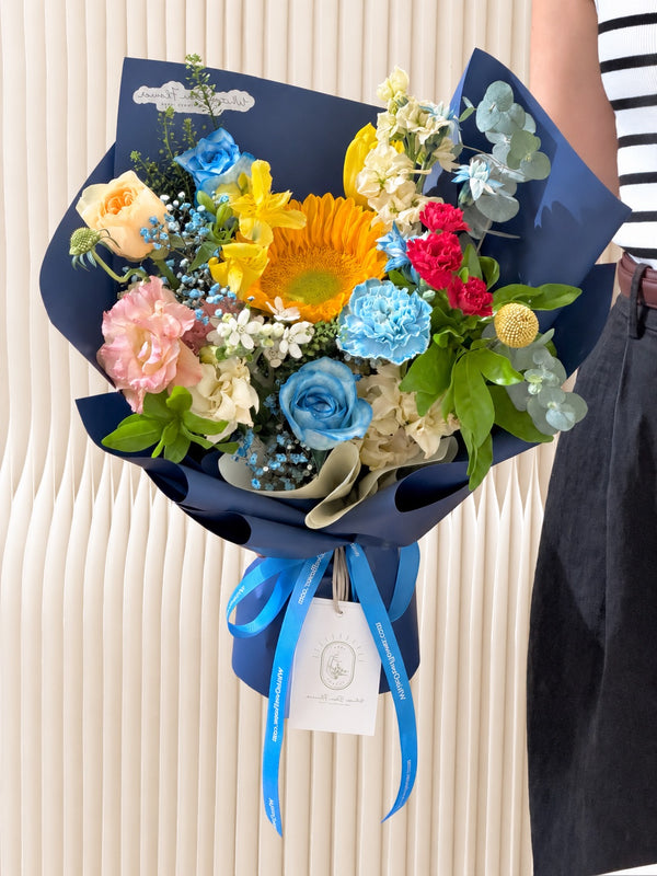Close-up of Bold Horizons graduation bouquet with sunflower, blue roses, blue carnation, yellow alstroemeria and colourful seasonal flowers.