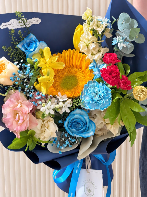 Bold Horizons graduation bouquet for men featuring sunflower, blue roses, yellow flowers and navy blue wrapping by White Dew Flower Singapore.