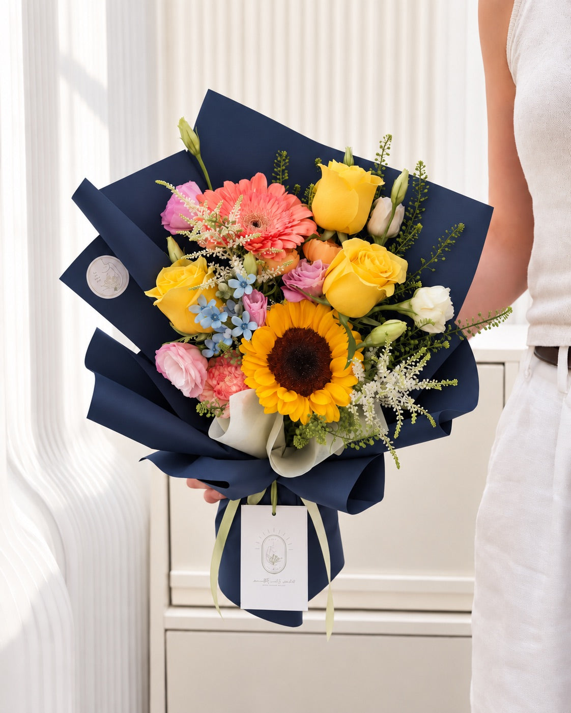 Colourful graduation bouquet featuring sunflower, yellow roses, pink lisianthus, white astilbe and blue oxypetalum in elegant navy wrapping.